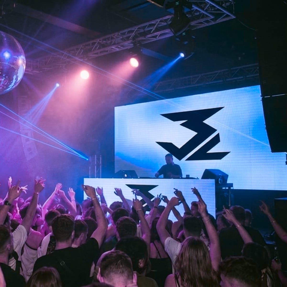 Vyprodaný parket na akci 3Lwave — dav se zvednutýma rukama a logo 3Lwave na LED stěně za DJ pultem